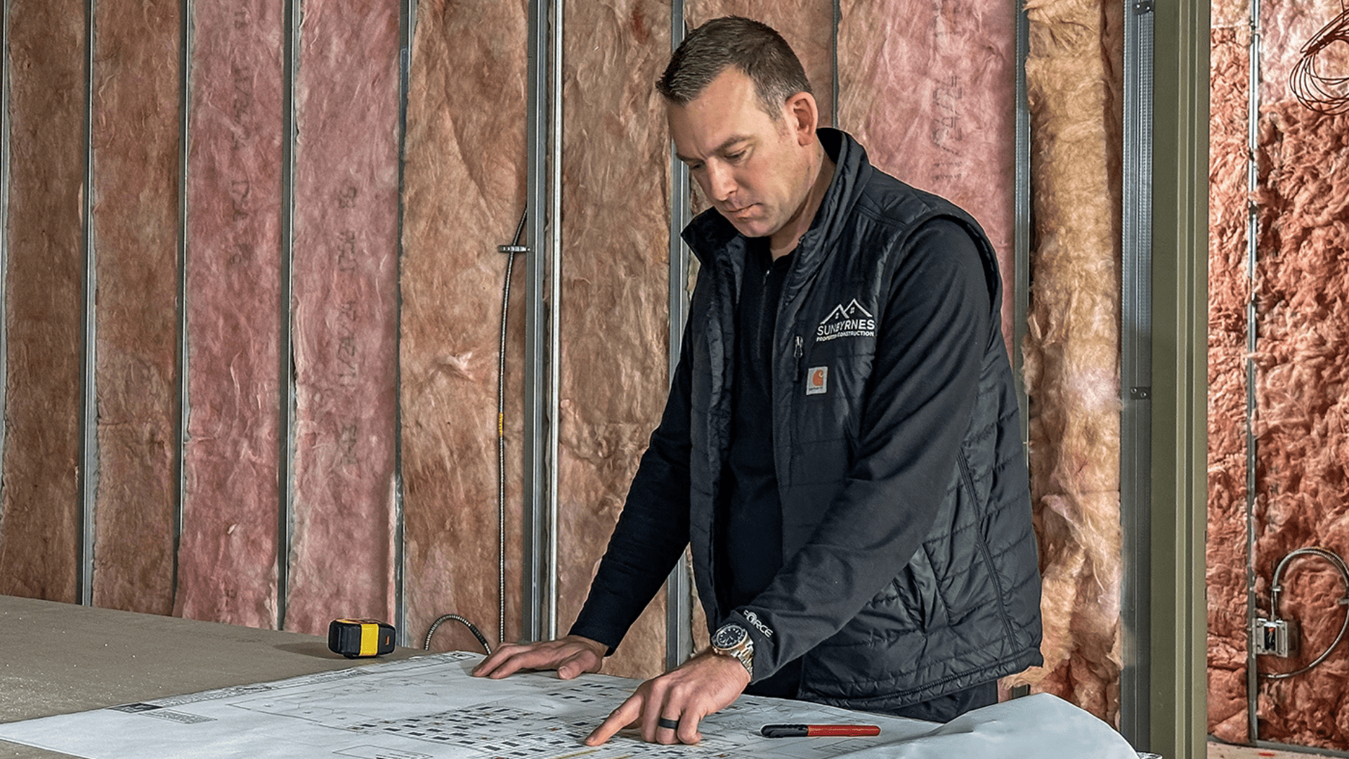 Brad Byrnes reviewing blueprints on a construction site, focused on every detail as he plans the next phase of a project. | Construction planning and development process in Michigan.