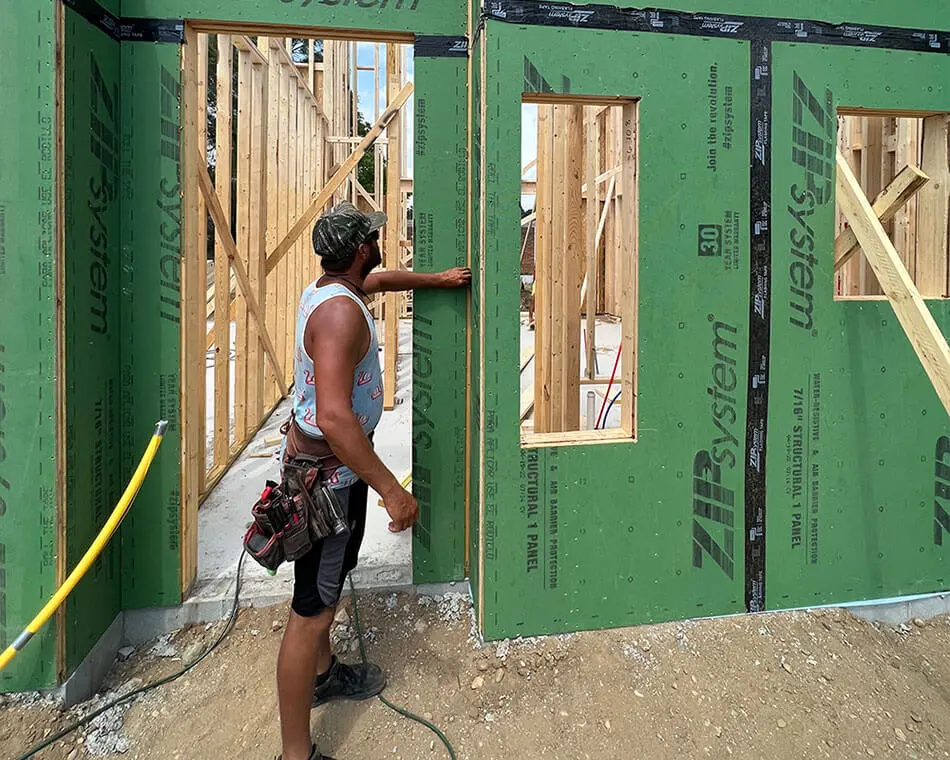 A construction worker inspecting framed wall openings on a new building exterior sheathed in green ZIP System structural panels.